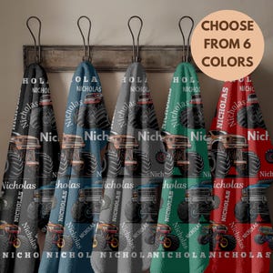 May include: Six colorful towels with a monster truck design and the name "Nicholas" printed on them. The towels are hanging on a wooden rack. The text "CHOOSE FROM 6 COLORS" is in a circle.