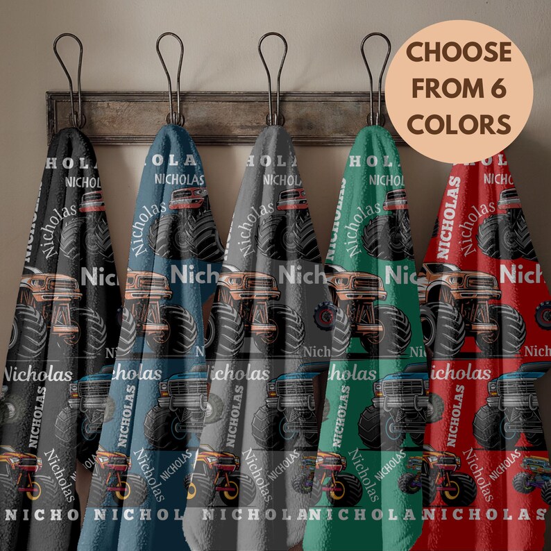 May include: Six colorful towels with a monster truck design and the name "Nicholas" printed on them. The towels are hanging on a wooden rack. The text "CHOOSE FROM 6 COLORS" is in a circle.