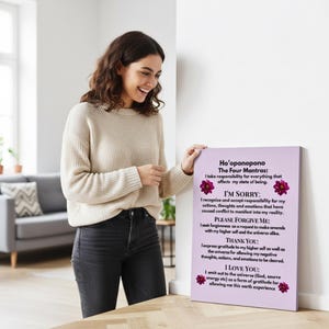 Op de afbeelding: Lichtpaarse canvas print met de tekst "Ho'oponopono The Four Mantras" in zwart, met bloemaccenten. Een persoon in een cr&egrave;mekleurige trui en zwarte jeans houdt de print vast.