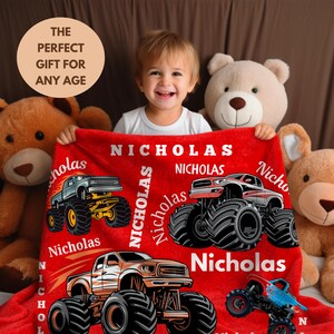 May include: A red blanket featuring monster truck graphics and the name "Nicholas" in white. The blanket has four different monster truck designs. The text "THE PERFECT GIFT FOR ANY AGE" is in a circle in the upper left corner.