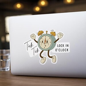 May include: A sticker featuring a vintage-style alarm clock character with arms and legs. The clock is light blue with brown accents and a smiling face. Text on the sticker includes "Tick Tick" and "LOCK IN O'CLOCK".