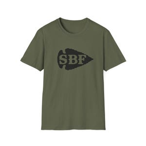 May include: An olive green short-sleeve t-shirt featuring a black arrowhead graphic centered on the chest. The letters SBF are printed in olive green inside the black arrowhead shape, creating a bold contrast against the solid fabric color.