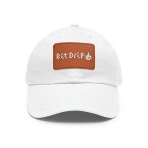 Puede incluir: Gorra de béisbol blanca con un parche de cuero marrón que dice "Bit Drip" en letras blancas pixeladas.