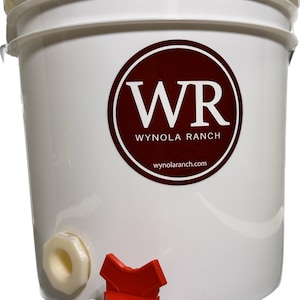 May include: White plastic bucket with a red and white logo that says "WR Wynola Ranch wynolaranch.com". The bucket has a white spigot with a red handle.