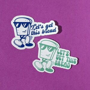 May include: Two stickers featuring a cartoon loaf of bread wearing sunglasses and walking. The text on the stickers reads "Let's get this bread". One sticker is blue and the other is green.