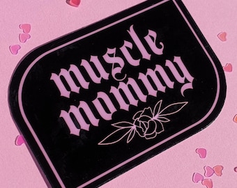 May include: Black and pink sticker with the text "muscle mommy" in a gothic font. A small flower design is below the text.