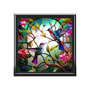 May include: A square, framed stained-glass panel featuring two hummingbirds perched on a branch. The birds have vibrant blue, green, and purple plumage. The background includes colorful flowers and foliage, with a black frame.