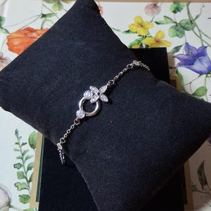 Peut inclure: Un bracelet à chaîne argentée doté d'un pendentif central en forme de fleur orné de petites pierres claires et d'un anneau circulaire. La fine chaîne métallique intègre également de petites pierres rondes dans son design.