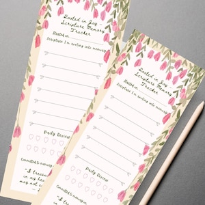 May include: Two beige scripture memory trackers with pink floral accents and the text "Rooted in Joy - Scripture Memory Tracker." Each tracker includes spaces for daily review and a quote from Psalm 119:11. A wooden pencil rests beside them.