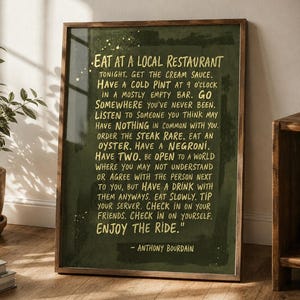Könnte beinhalten: Ein gerahmter Kunstdruck mit dunkelgrünem, texturiertem Hintergrund und goldfarbenem Text. Der Text lautet: EAT AT A LOCAL RESTAURANT TONIGHT. GET THE CREAM SAUCE. HAVE A COLD PINT AT 9 O'CLOCK IN A MOSTLY EMPTY BAR. GO SOMEWHERE YOU'VE NEVER BEEN. LISTEN TO SOMEONE YOU THINK MAY HAVE NOTHING IN COMMON WITH YOU. ORDER THE STEAK RARE. EAT AN OYSTER. HAVE A NEGRONI. HAVE TWO. BE OPEN TO A WORLD WHERE YOU MAY NOT UNDERSTAND OR AGREE WITH THE PERSON NEXT TO YOU, BUT HAVE A DRINK WITH THEM ANYWAYS. EAT SLOWLY. TIP YOUR SERVER. CHECK IN ON YOUR FRIENDS. CHECK IN ON YOURSELF. ENJOY THE RIDE. - ANTHONY BOURDAIN