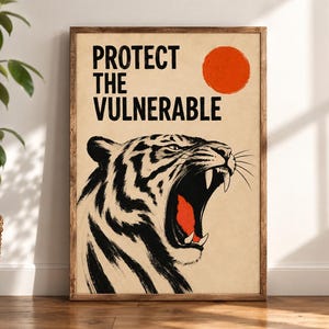 May include: A rectangular wall art print in a wooden frame featuring a black and white illustration of a roaring tiger with an open mouth showing red accents. The text PROTECT THE VULNERABLE is printed in black above a solid orange circle on a beige background.