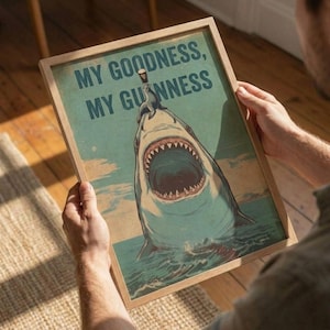 May include: A framed print with the text "MY GOODNESS, MY GUINNESS" in blue letters. The image depicts a shark with an open mouth, and a seal balancing a pint of Guinness on its nose. The background is a teal color.