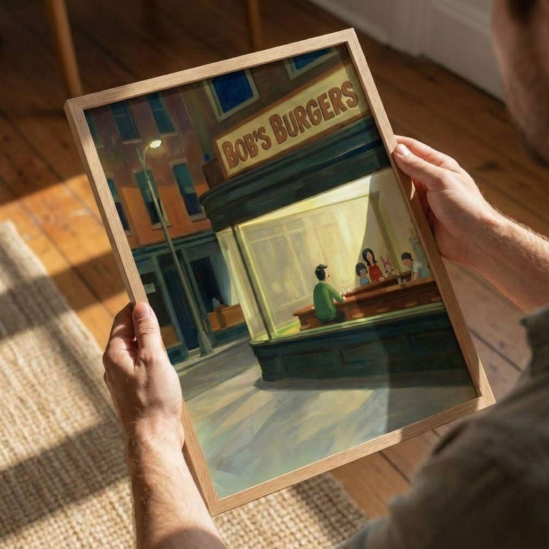 May include: A framed print of a painting depicting a diner scene at night. The diner is lit up, with the words "Bob's Burgers" above the entrance. A person sits at the counter, and other figures are visible inside. The background shows a street with buildings.