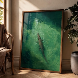 Könnte beinhalten: Ein rechteckiger Wandkunstdruck in einem dunklen Holzrahmen mit einer Luftaufnahme eines Krokodils, das in leuchtend grünem Wasser schwimmt. Das Kunstwerk zeigt das Reptil mittig im Rahmen, umgeben von wirbelnden Wellen im tiefen smaragdgrünen Wasser.