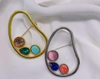 Broche contemporáneo con forma abstracta geométrica y piedras de colores en plata y oro. Accesorios minimalistas