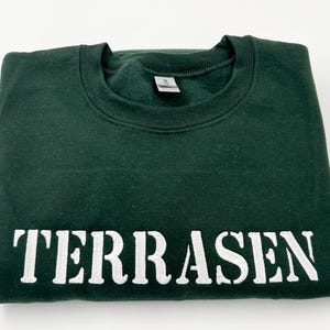 May include: A dark green sweatshirt with the word "TERRASEN" printed in white on the front.