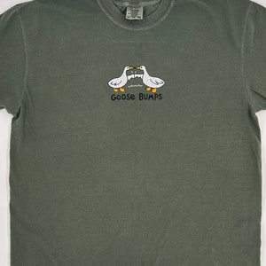 May include: A dark green t-shirt with a white graphic of two geese facing each other with the text "Goose Bumps" underneath.