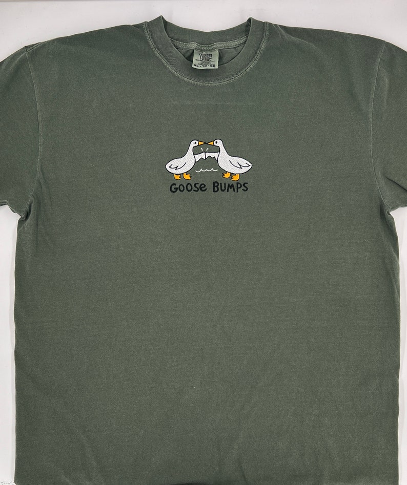 May include: A dark green t-shirt with a white graphic of two geese facing each other with the text "Goose Bumps" underneath.