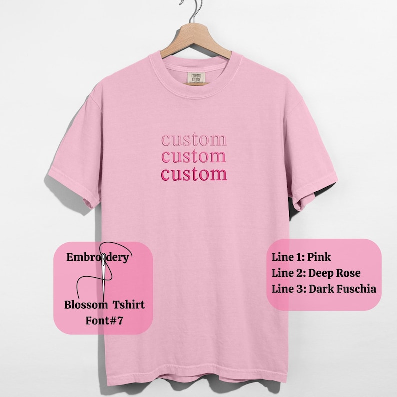 May include: A light pink t-shirt with the word "custom" embroidered three times in varying shades of pink. The shirt is hanging on a wooden hanger. The text "Embroidery, Blossom Tshirt, Font#7" is also visible.