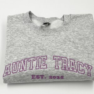 May include: Gray sweatshirt with purple embroidered text that reads "Auntie Tracy Est. 2023".