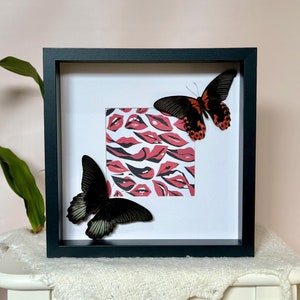 May include: A black framed picture with a white mount and a print of red lips. Two butterflies are mounted on the print, one black and one orange and black.