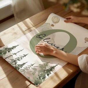 May include: A watercolour print featuring a green circle with the name "Oliver" written in cursive. The background features a watercolour illustration of a forest with trees and a hot air balloon.