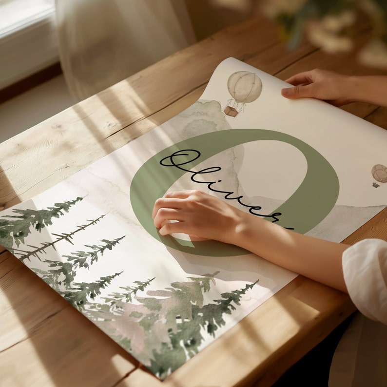 May include: A watercolour print featuring a green circle with the name "Oliver" written in cursive. The background features a watercolour illustration of a forest with trees and a hot air balloon.