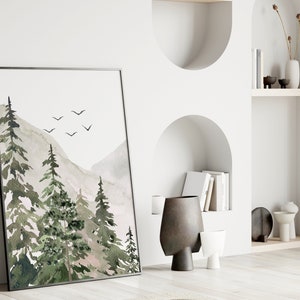 May include: A framed watercolour painting of a mountain landscape with green trees and a light grey sky. There are a few small black birds flying in the sky.