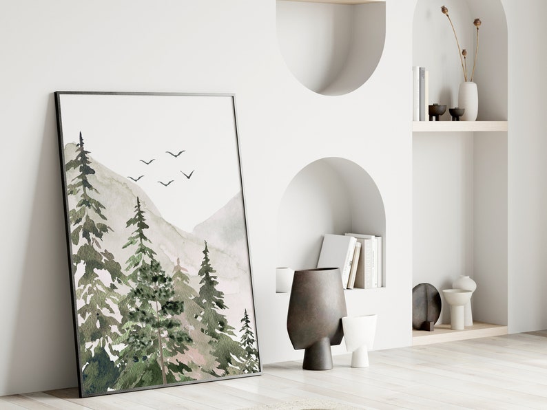May include: A framed watercolour painting of a mountain landscape with green trees and a light grey sky. There are a few small black birds flying in the sky.