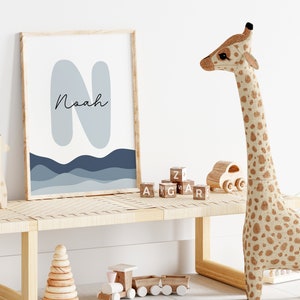 May include: A framed print with a blue and gray abstract design featuring the letter "N" and the name "Noah". The print is displayed on a wooden shelf with a stuffed giraffe toy, wooden blocks, and a wooden toy train.