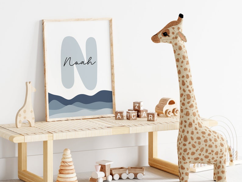 May include: A framed print with a blue and gray abstract design featuring the letter "N" and the name "Noah". The print is displayed on a wooden shelf with a stuffed giraffe toy, wooden blocks, and a wooden toy train.