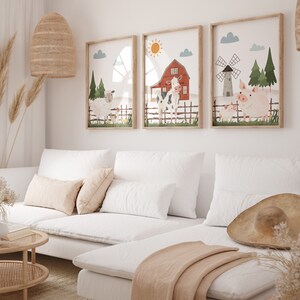 May include: Three framed illustrations of farm animals, including a cow, pig, and sheep, with a red barn and windmill in the background. The illustrations are in a white room with a white sofa and a brown hat on the sofa.