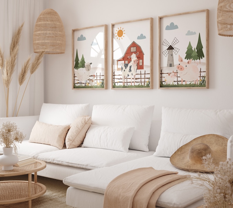 May include: Three framed illustrations of farm animals, including a cow, pig, and sheep, with a red barn and windmill in the background. The illustrations are in a white room with a white sofa and a brown hat on the sofa.