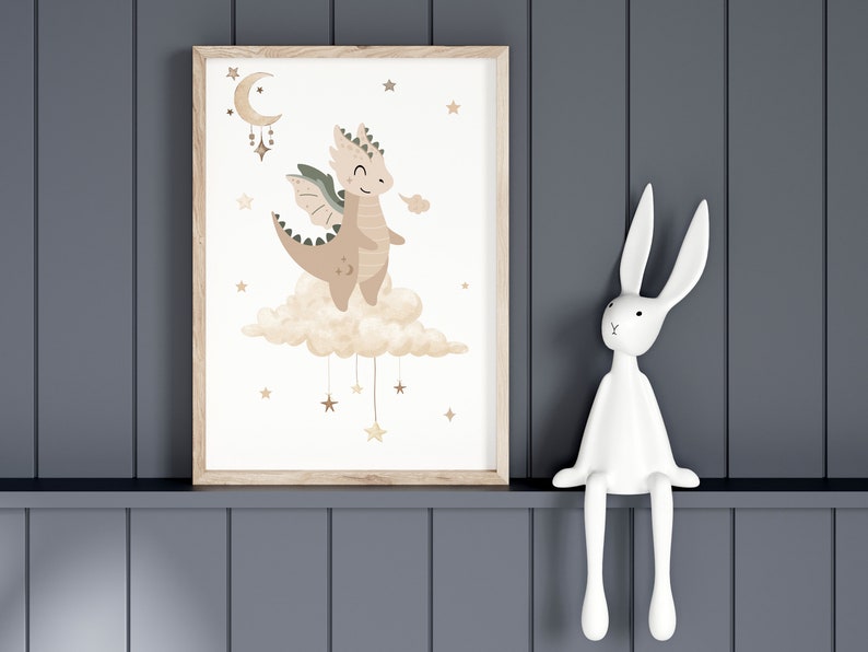 May include: A framed print of a cartoon dragon with brown and green wings, sitting on a cloud with stars hanging from it. The dragon is smiling and has a light brown body with a light brown cloud behind it. The background is white with gold stars.