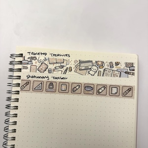 Puede incluir: Un cuaderno blanco con un patr&oacute;n de puntos marrones. El cuaderno tiene una encuadernaci&oacute;n en espiral y un borde de cinta washi marr&oacute;n y blanco con el texto "Tabletop Treasures" y "Stationary Toolbar". La cinta washi presenta ilustraciones de art&iacute;culos de oficina.