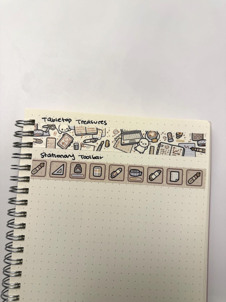 Puede incluir: Un cuaderno blanco con un patr&oacute;n de puntos marrones. El cuaderno tiene una encuadernaci&oacute;n en espiral y un borde de cinta washi marr&oacute;n y blanco con el texto "Tabletop Treasures" y "Stationary Toolbar". La cinta washi presenta ilustraciones de art&iacute;culos de oficina.