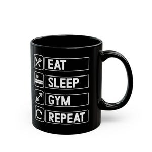 Op de afbeelding: Zwarte koffiemok met witte tekst die "Eten, Slapen, Gym, Herhalen" luidt.