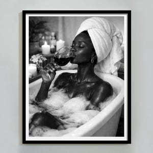 May include: Monochrome framed print showing a person in a bathtub, drinking red wine. They are wearing a white towel on their head and surrounded by bubbles. Candles and flowers are visible in the background.