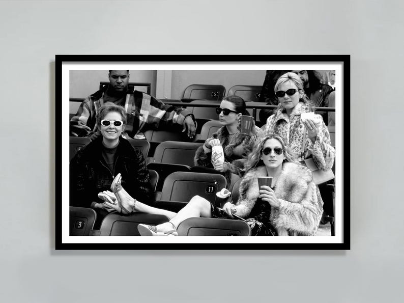 May include: Black and white framed photograph of a group of people in a stadium setting. The subjects are wearing sunglasses and fur coats. The image is a candid shot, capturing a moment in time.