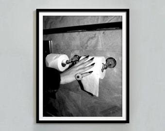 Op de afbeelding: Een zwart-witfoto van een hand die naar een rol toiletpapier reikt. De hand draagt een ring met een grote steen.