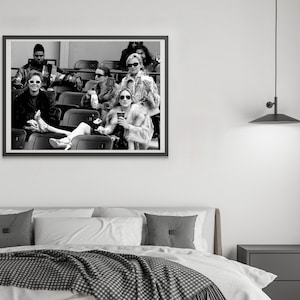 May include: Black and white framed photograph of a group of people in an outdoor setting. The subjects are seated in stadium seating, wearing sunglasses and fashionable clothing. The image is a medium shot, capturing the group's expressions and attire.