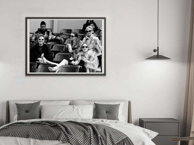 May include: Black and white framed photograph of a group of people in an outdoor setting. The subjects are seated in stadium seating, wearing sunglasses and fashionable clothing. The image is a medium shot, capturing the group's expressions and attire.