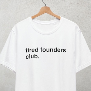 Puede incluir: Camiseta blanca con el texto "tired founders club." impreso en negro.
