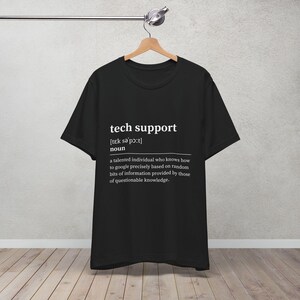 Op de afbeelding: Zwart t-shirt met de woorden "tech support" en de fonetische uitspraak in het wit. Daaronder beschrijft een definitie een getalenteerd persoon die precies kan googelen.
