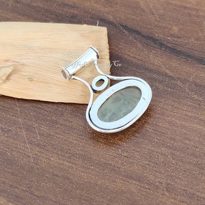 May include: Silver pendant with a green oval gemstone set in a silver bezel. The pendant has a bail with a loop at the top.
