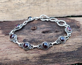 May include: A silver bracelet with a chain link design and six red gemstone accents.