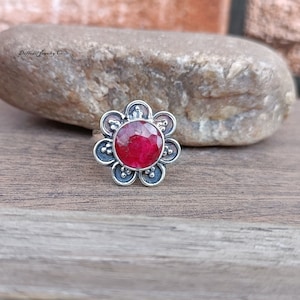 May include: A silver ring with a red ruby gemstone set in a flower-shaped design.