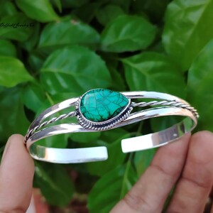 May include: A silver bangle bracelet with a green turquoise stone set in a silver bezel. The bracelet has a twisted wire design.