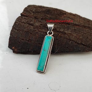 May include: A silver pendant with a turquoise stone in a rectangular shape. The pendant has a rope-like border around the stone.