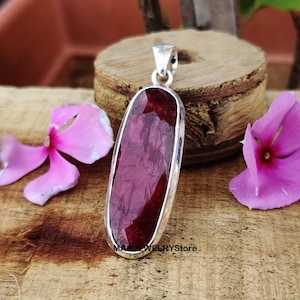 Könnte beinhalten: Ein silberner Anhänger mit einem großen, ovalen, facettierten Rubin-Edelstein. Der Anhänger ist in einer silbernen Fassung gefasst und hat eine Öse zum Anbringen an einer Kette.